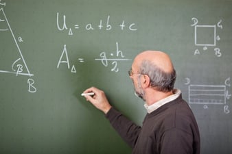 Male teacher writes on blackboard with a chalk
